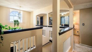 A spacious interior with a high ceiling, a balcony with a railing, and a staircase leading to an upper floor. - Air Hockey, Pool, Fireplace, Basketball, & more! (El Paso)
