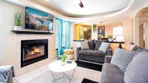 A modern living room with a fireplace, a ceiling fan, and a sofa. - Air Hockey, Pool, Fireplace, Basketball, & more! (El Paso)