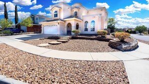 A two-story house with a driveway, a front yard with a stone pathway, and a clear blue sky. - Air Hockey, Pool, Fireplace, Basketball, & more! (El Paso)