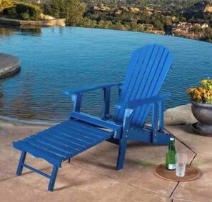A blue Adirondack chair by a pool with a view of a hilly landscape.
