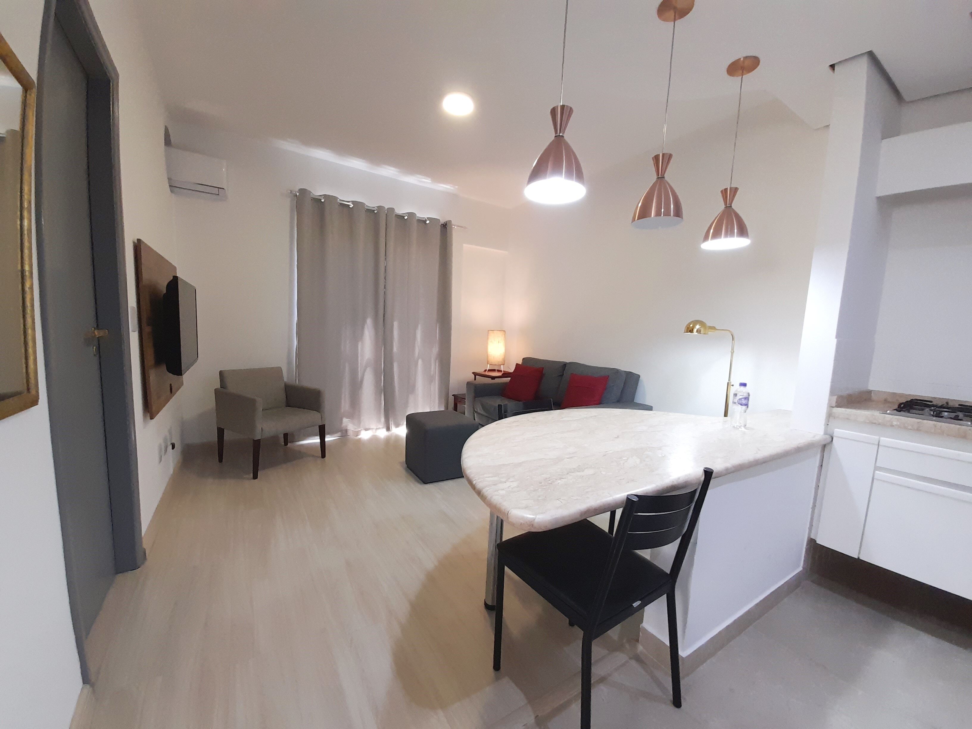 Un espacio de estar moderno con comedor, un sofá, un televisor montado en la pared y una cocina con estufa.
