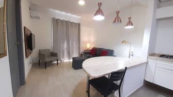 Un espacio de estar moderno con comedor, un sofá, un televisor montado en la pared y una cocina con estufa.
