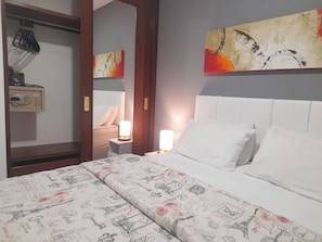 Quarto de hotel com uma cama, uma mesa de cabeceira com abajur, um guarda-roupa e um quadro na parede.