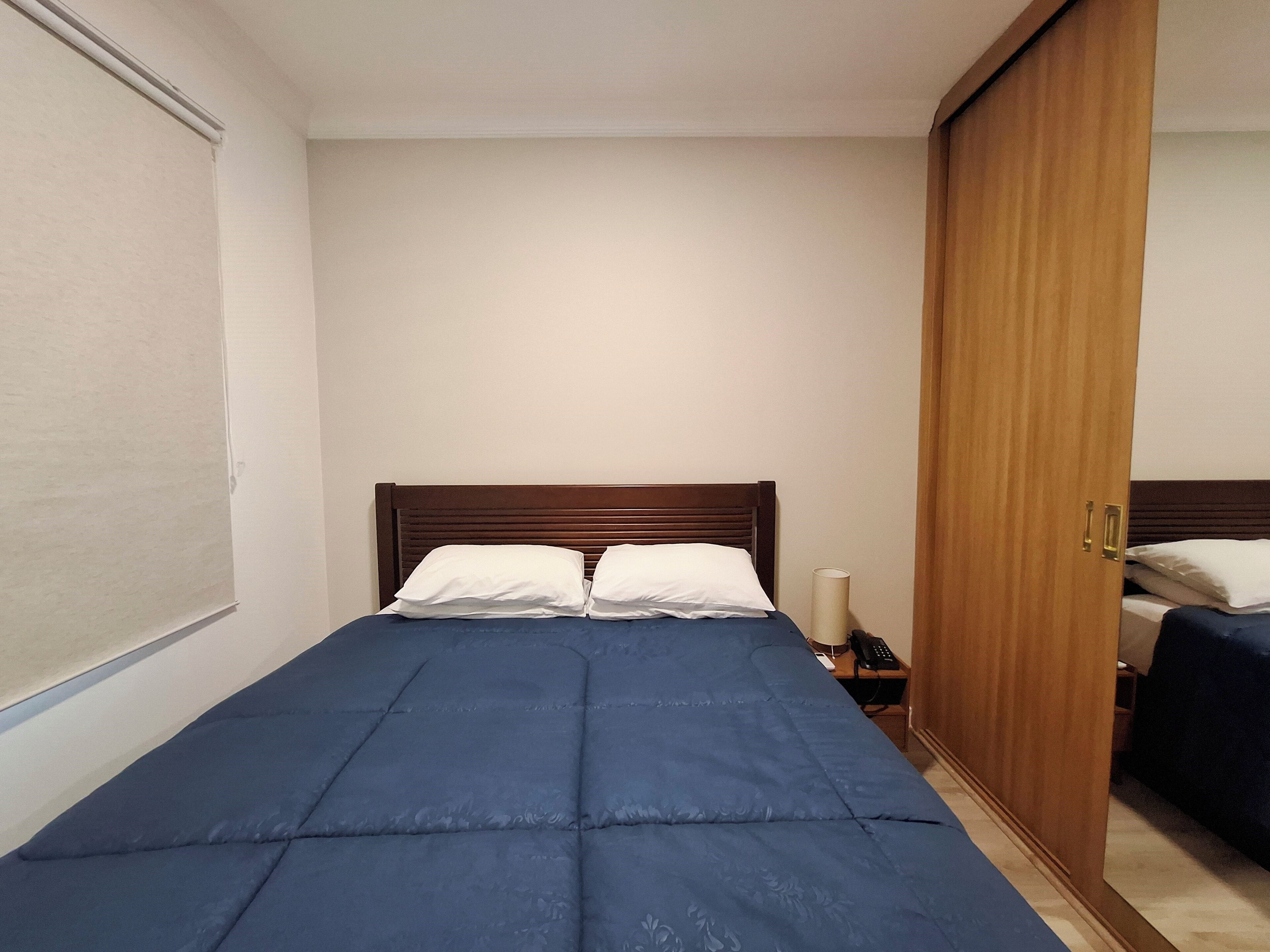 Un dormitorio con cama, armario de madera y mesita de noche con lámpara y teléfono.
