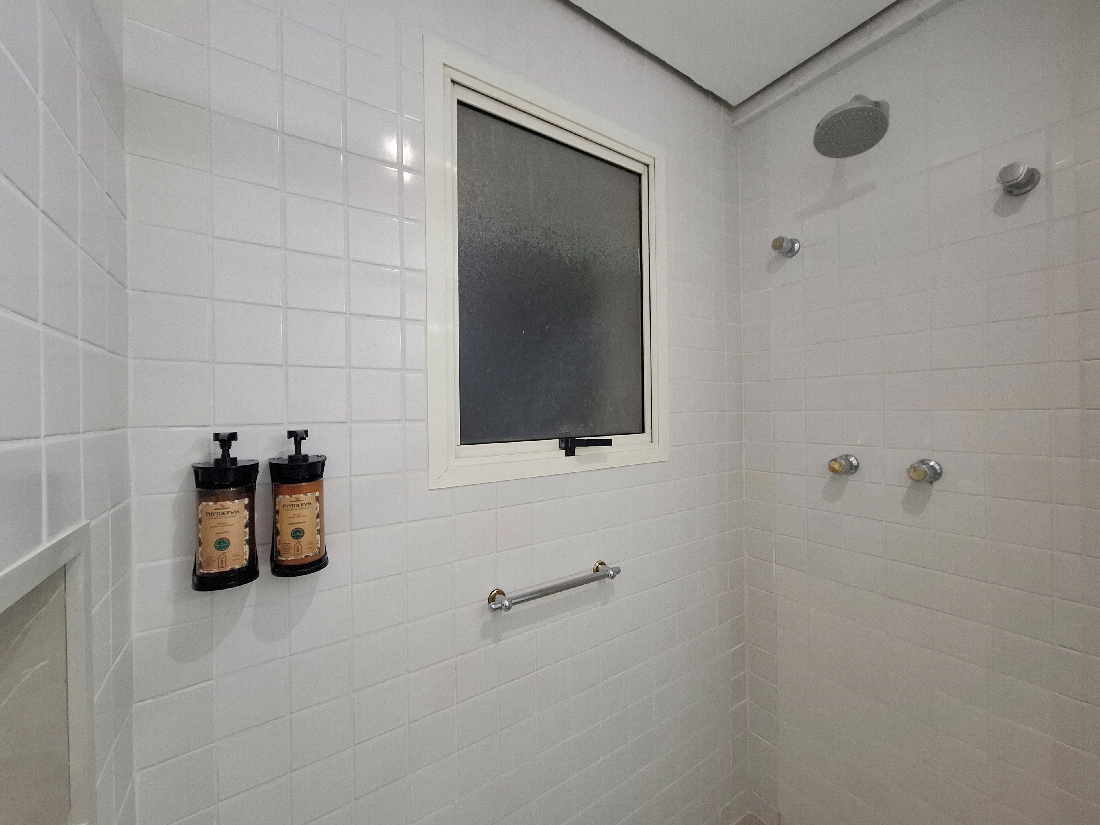 Une douche avec une fenêtre, des murs recouverts de carreaux blancs et deux bouteilles de shampoing.
