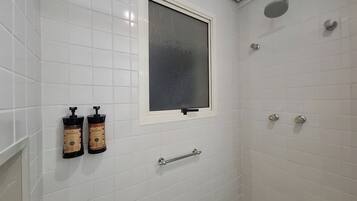 Une douche avec une fenêtre, des murs recouverts de carreaux blancs et deux bouteilles de shampoing.