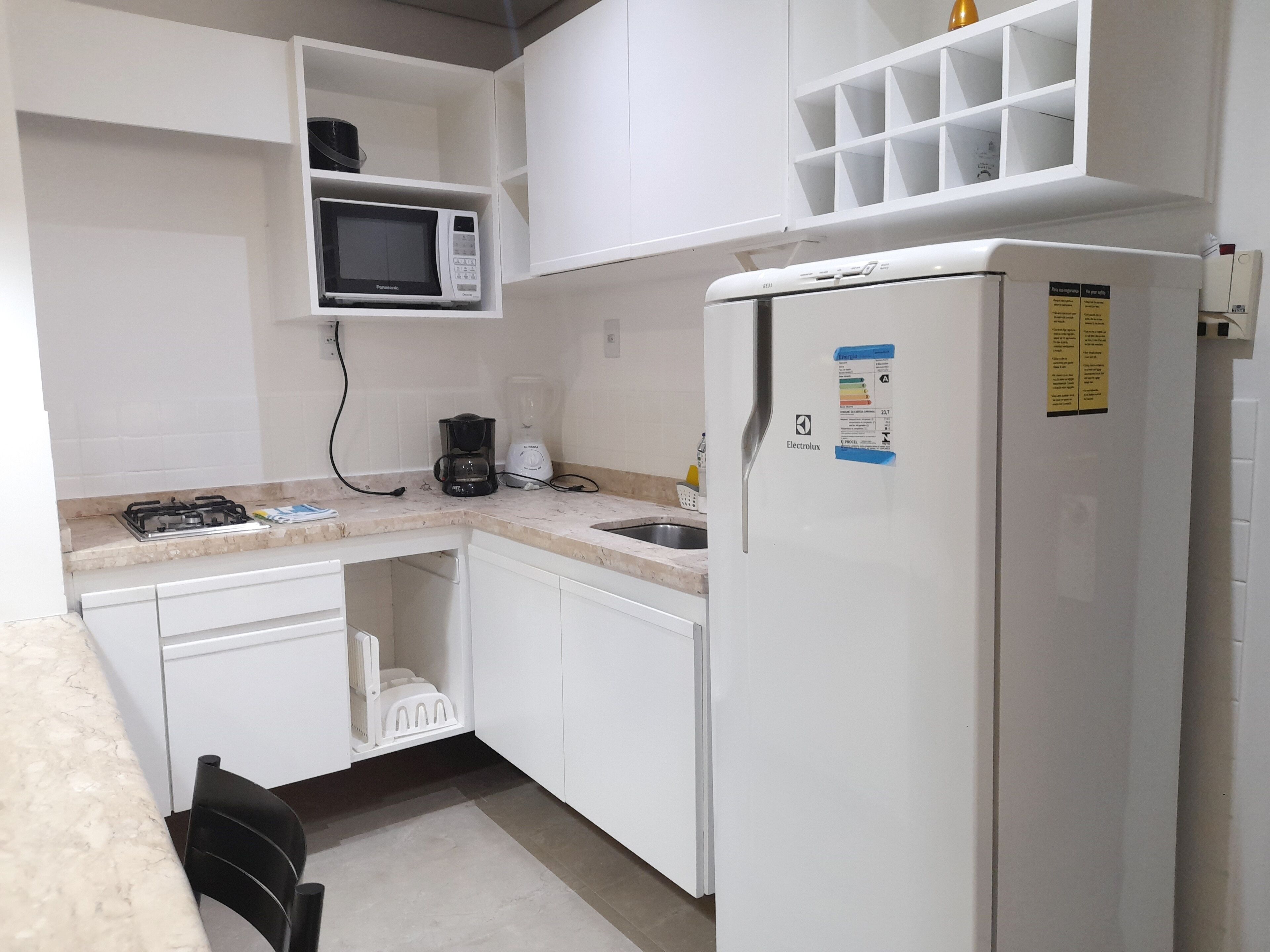 Une cuisine de taille réduite, dotée de meubles blancs, d’un four à micro-ondes, d’un mixeur, d’un réfrigérateur et d’une cuisinière à gaz.