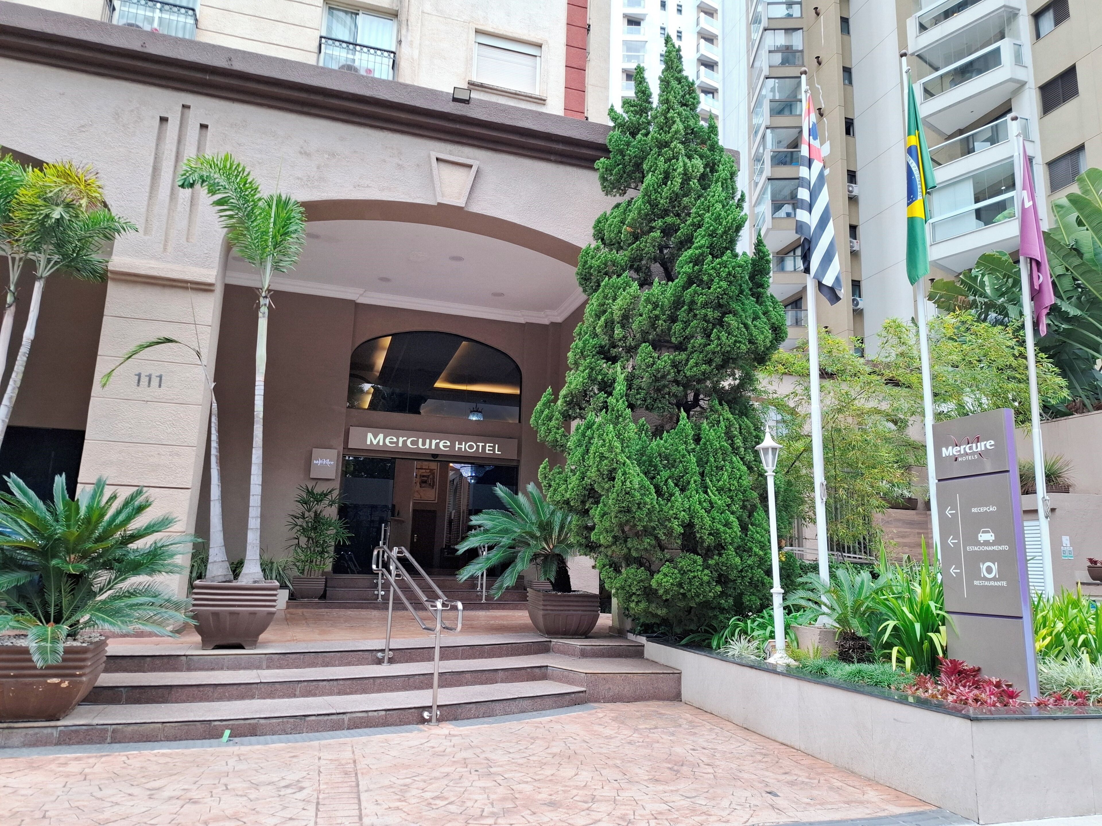 The entrance to Mercure Hotel with a staircase, potted plants, and flags.