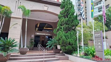 The entrance to Mercure Hotel with a staircase, potted plants, and flags.