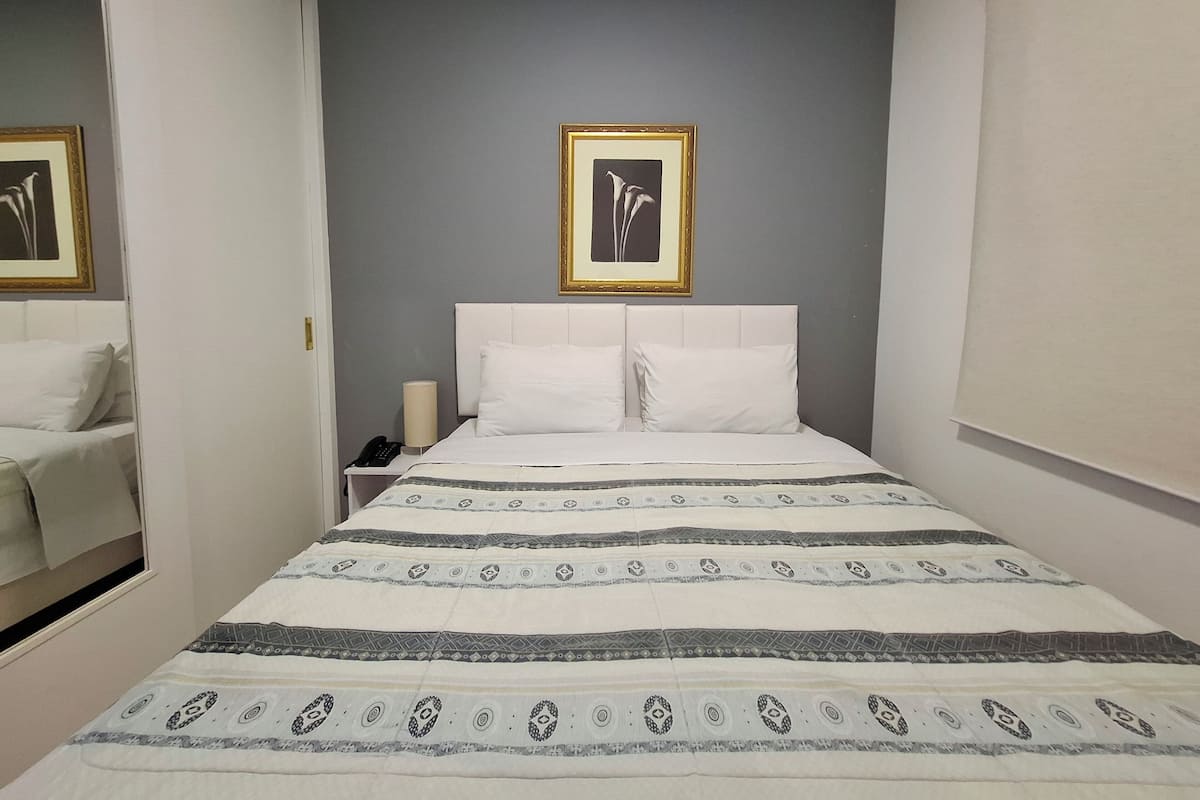 Habitació d'hotel amb un llit, una taula de nit, una làmpada i un quadre al mur.