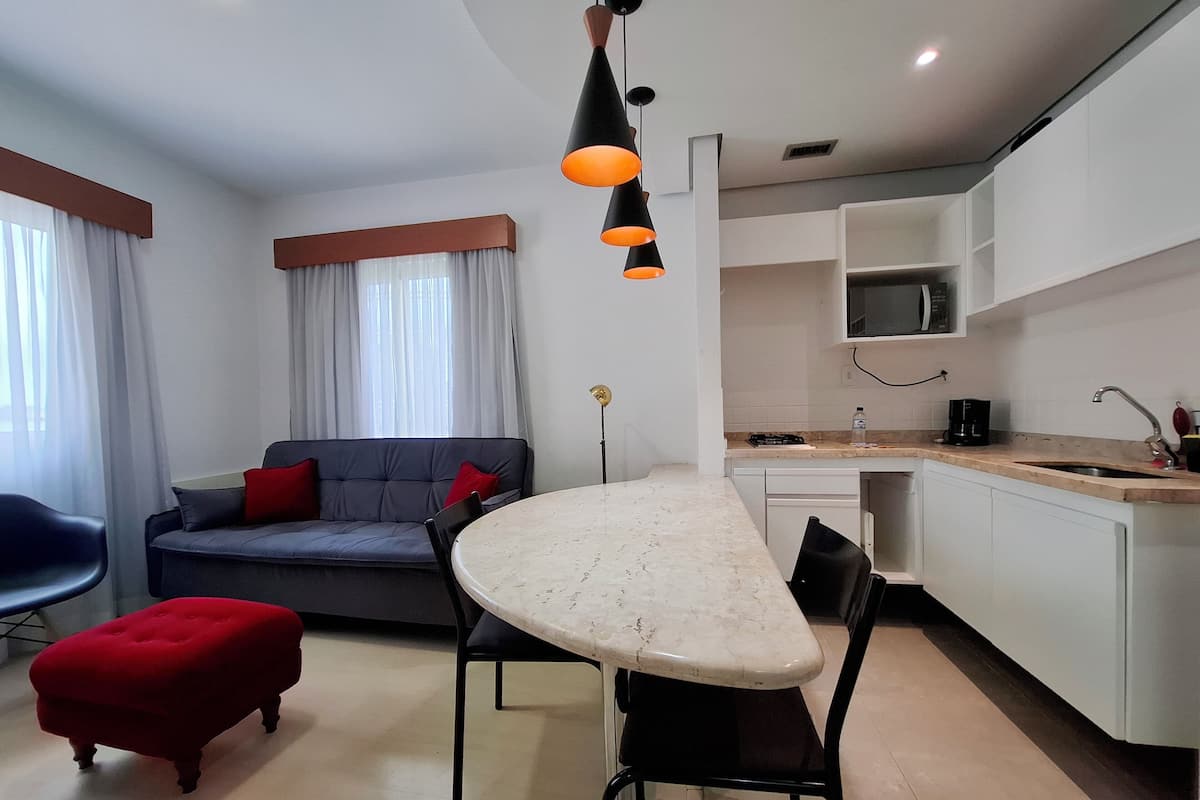Un saló modern amb un sofà, un petaca i una taula de menjador. Es pot veure una zona de cuina amb un microones i un rentaplat.