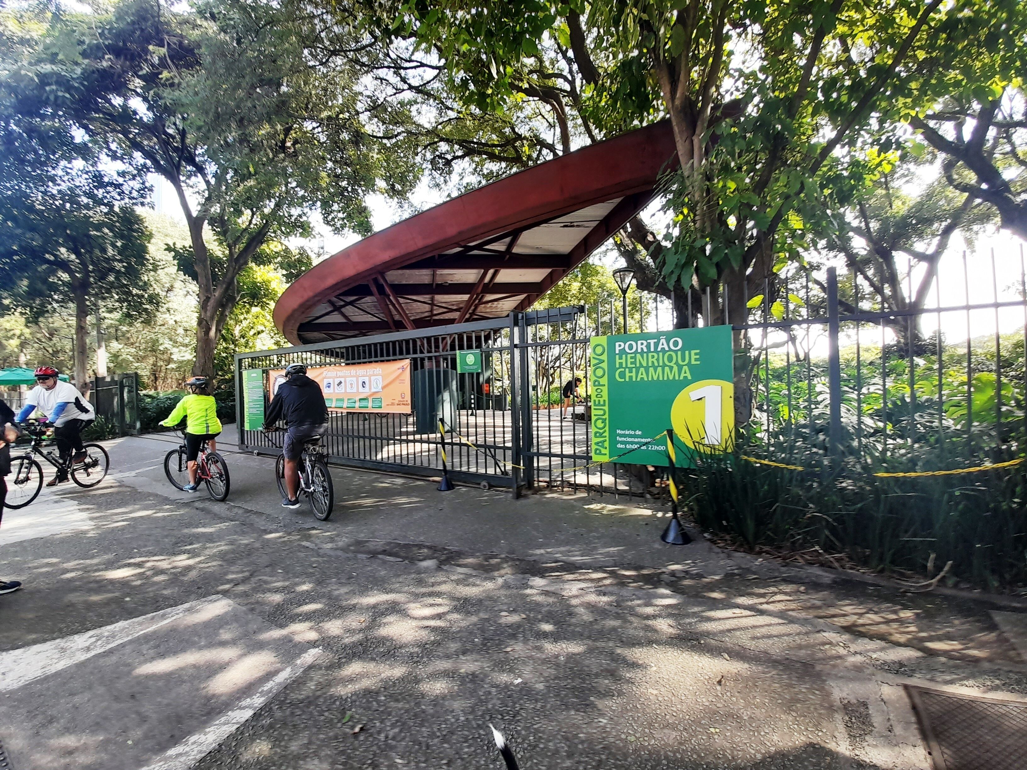 A covered bike parking area with a sign indicating 'Portão Henrique Chamma' and a green sign with a yellow circle.