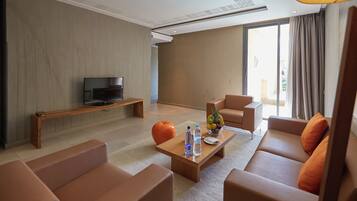 A modern living room with a sofa, a coffee table with water bottles, a fruit bowl, and a television on a wooden stand.
