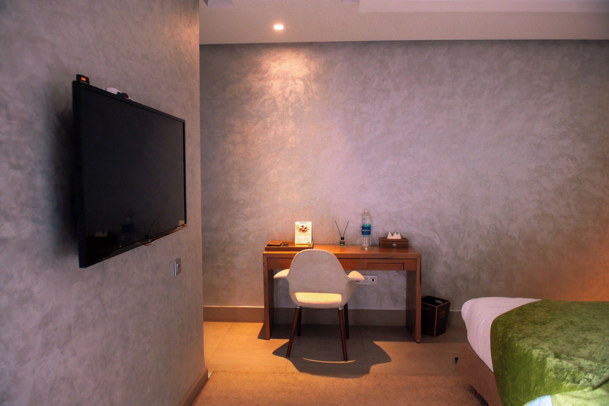 A hotel room with a bed, a desk with a chair, a television, and a small trash bin.