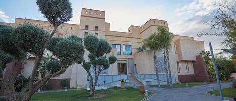A modern building with a symmetrical facade, a central entrance with steps, and a paved courtyard with neatly trimmed grass and trees.
