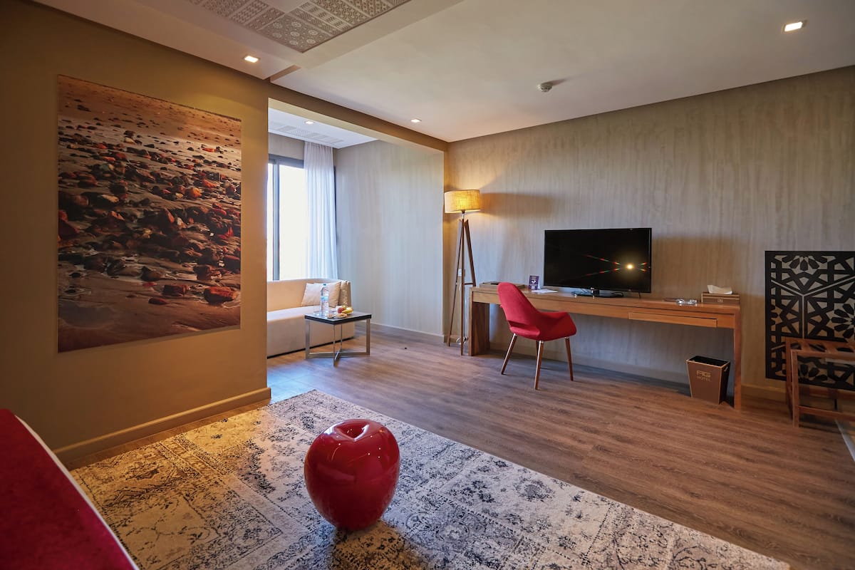 Una habitación de hotel moderna con un cuadro grande, un escritorio con computadora, un televisor y una silla roja.