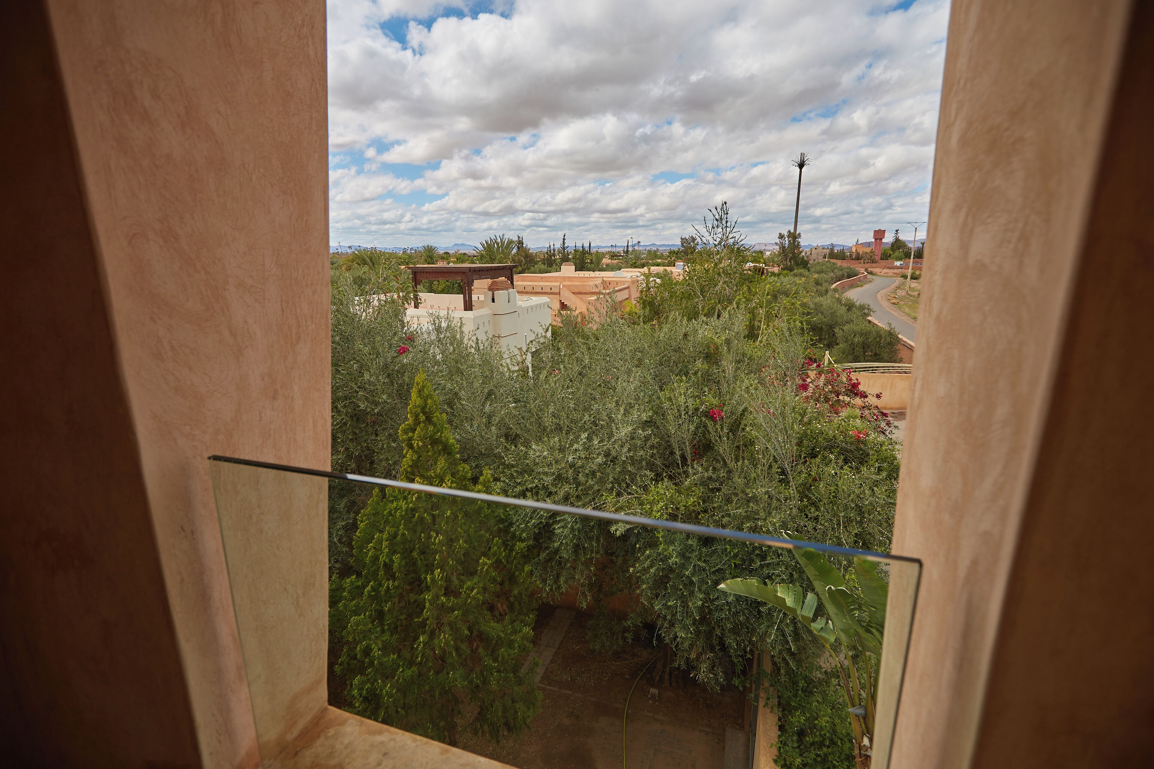 A view from a balcony with a railing, overlooking a landscaped area with various plants and a distant building structure.