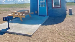 A cylindrical building with a blue door and windows, a picnic table, and a small air conditioning unit. - Up-cycled Grain Bin Villa just 20 mins. from the Great Sand Dunes NP w/ WiFi, AC (Mosca)