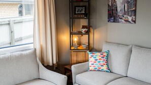 A living room with a grey sofa, a colorful pillow, a shelf with decorative items, and a painting on the wall. - Restful on Rhoboro - Free Wifi (Twizel)