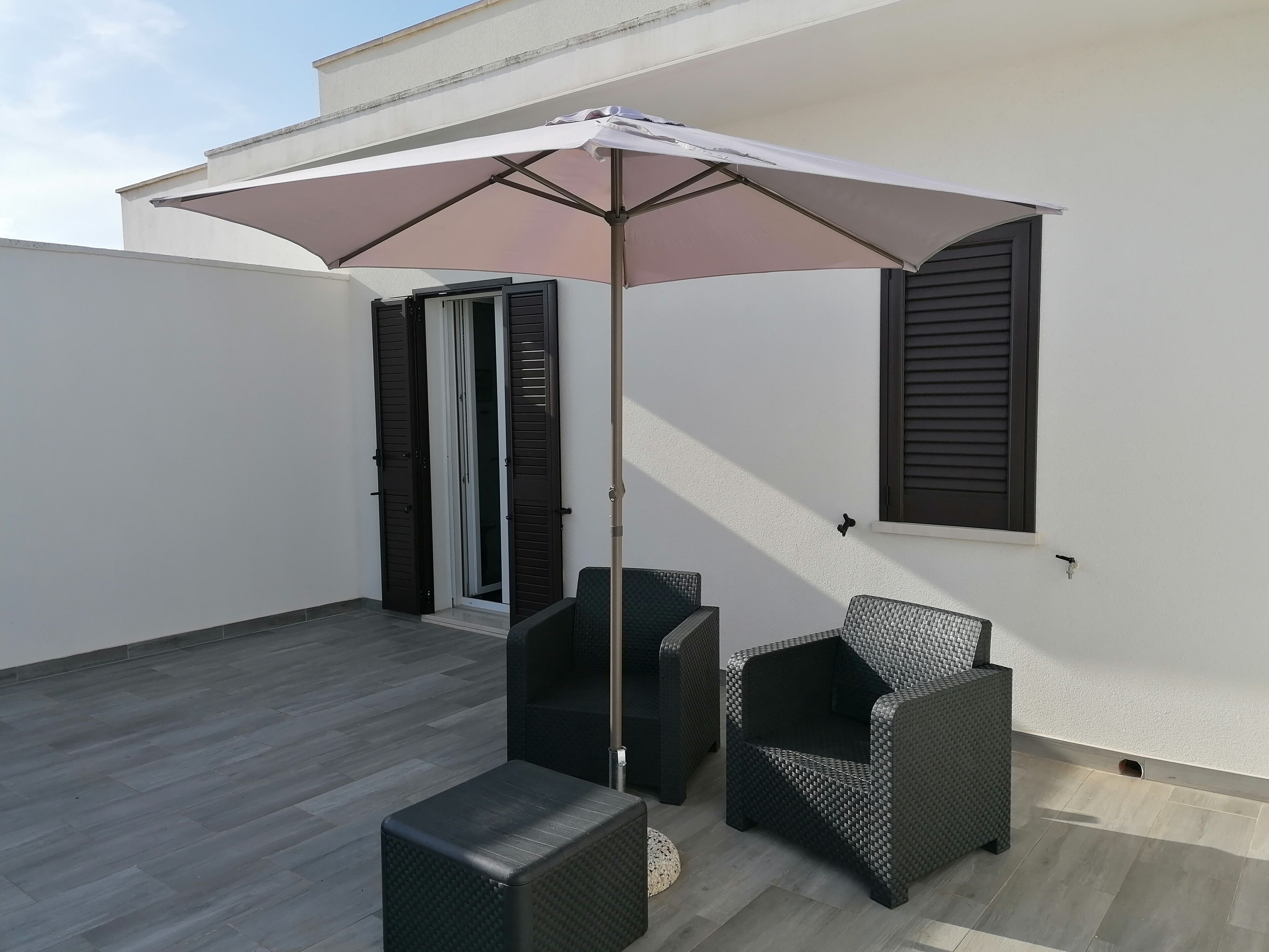 Un patio con dos sillas de mimbre, una mesita y un paraguas grande.