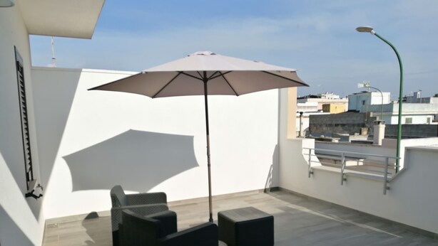 Una terraza en la azotea con un conjunto de patio que incluye una mesa, sillas y una gran sombrilla, además de una farola.