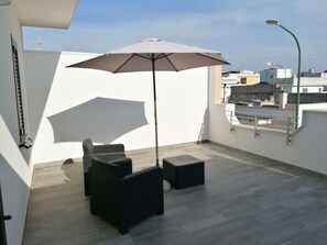Eine Dachterrasse mit Sitzgruppe, inklusive Tisch und Stühlen, einem großen Sonnenschirm und einer Straßenlaterne.