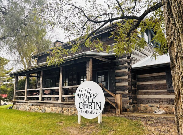 Une cabane en rondins avec un porche, une enseigne indiquant « Hébergement Hittop Cabin », et des fondations en pierre.