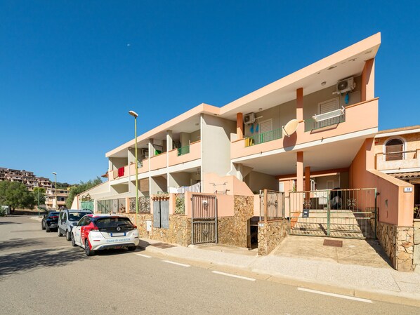 A multi-story residential building with balconies, a gated entrance, and a clear blue sky.