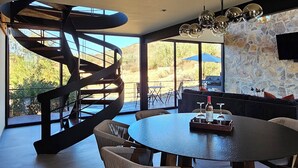 A modern dining area with a spiral staircase, large windows, and a stone wall. - CASA SEKUI (Valle de Guadalupe)