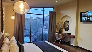 A spacious bedroom with a large bed, a desk, and a view of a mountainous landscape through the window. - CASA SEKUI (Valle de Guadalupe)