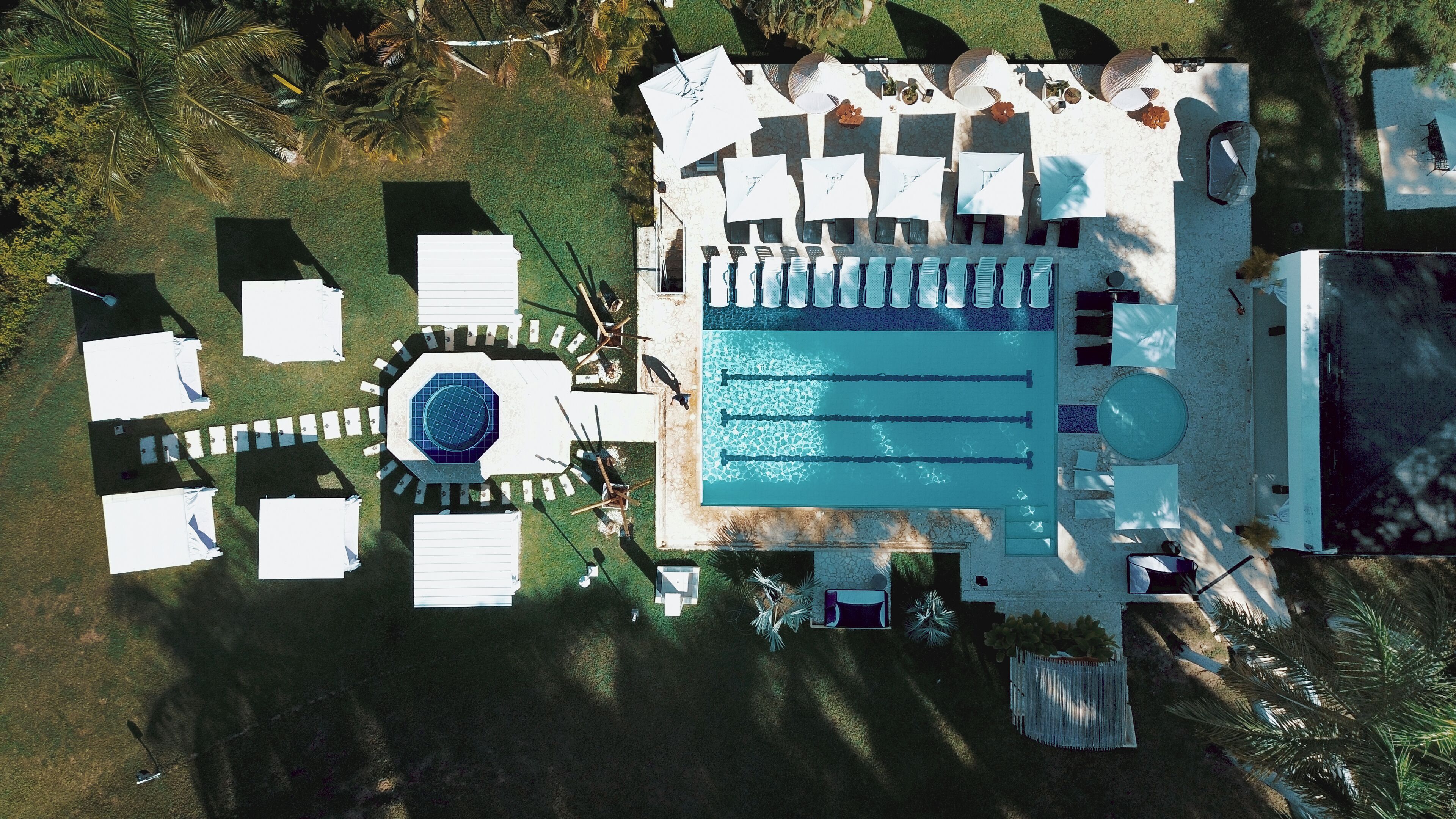 Vue aérienne d’un complexe hôtelier doté d’une piscine, de chaises longues et d’un espace de détente circulaire.