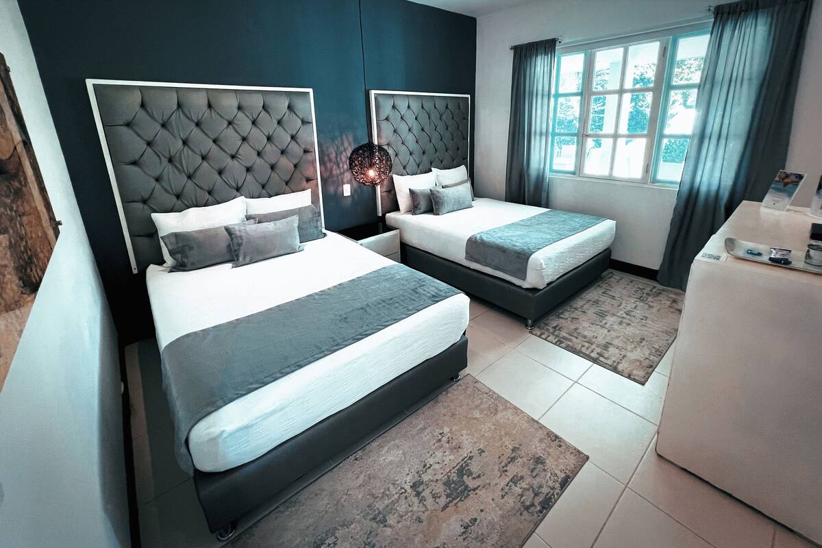 A modern hotel room with two beds, a desk, and a large window with curtains.