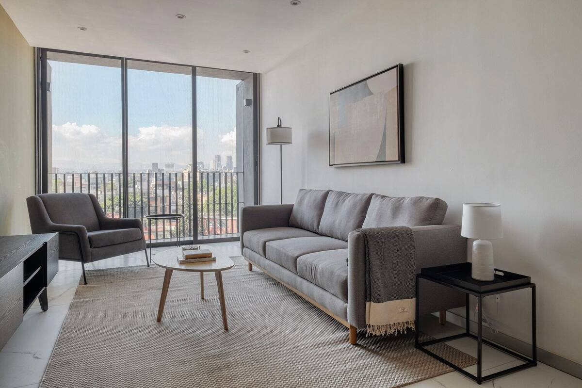A modern living room with a grey sofa, a black armchair, a small round table, and a black side table with a lamp.