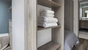 A modern bedroom with a wooden wardrobe, a bed with a grey patterned bedspread, and a bathroom visible through an open door. - Blueground Ava Rio Rhin in Mexico City (Mexico City)