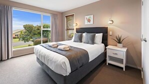Une chambre à coucher moderne avec un grand lit, une table de chevet avec une lampe et une vue sur l’extérieur.