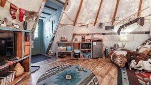 Una habitación tipo tienda de campaña, acogedora y rústica, con kitchenette, estantería y alfombra estampada.