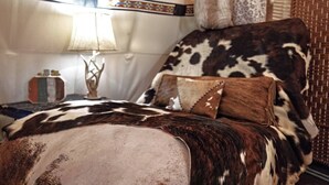 Una cama con funda de piel de vaca, una lámpara y un borde decorativo en la pared.