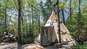 Una carpa rústica con una pequeña puerta de madera, rodeada por un bosque con una escultura de caballo y una estatua de oso.