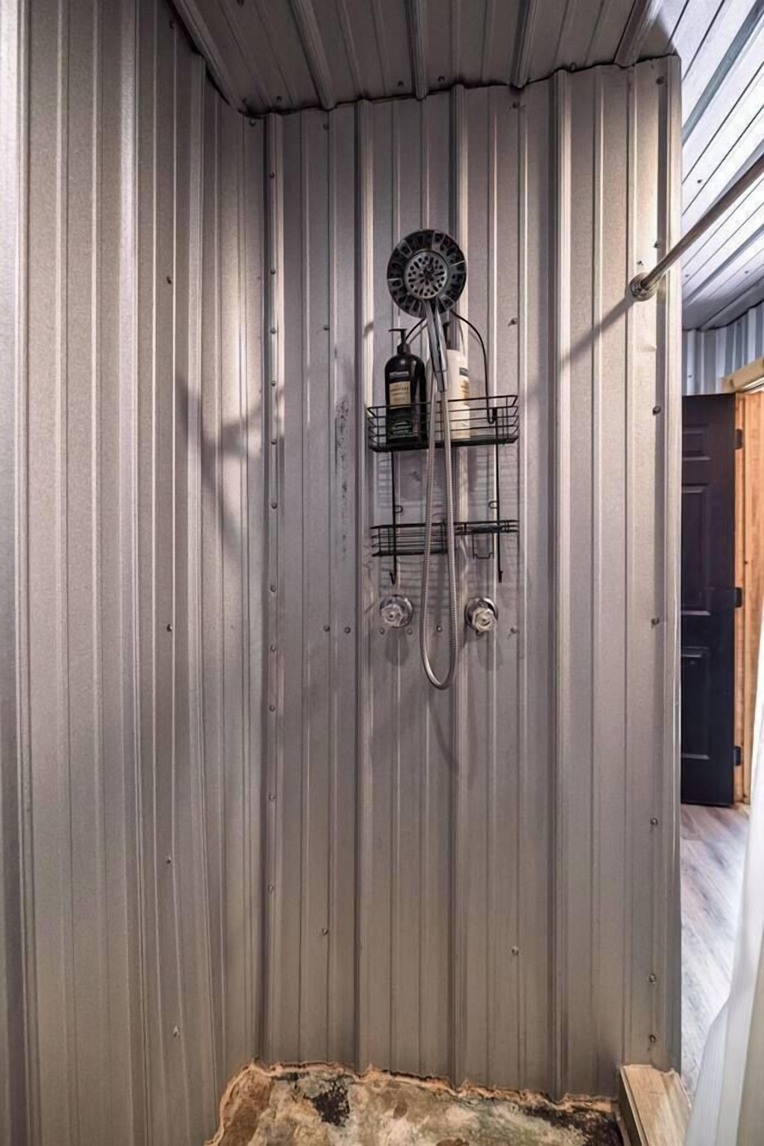 Une douche dotée d’un pommeau circulaire, d’un porte-savon et d’un porte-serviettes, le tout installé contre un mur en métal ondulé.