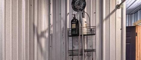 Une douche dotée d’un pommeau circulaire, d’un porte-savon et d’un porte-serviettes, le tout installé contre un mur en métal ondulé.