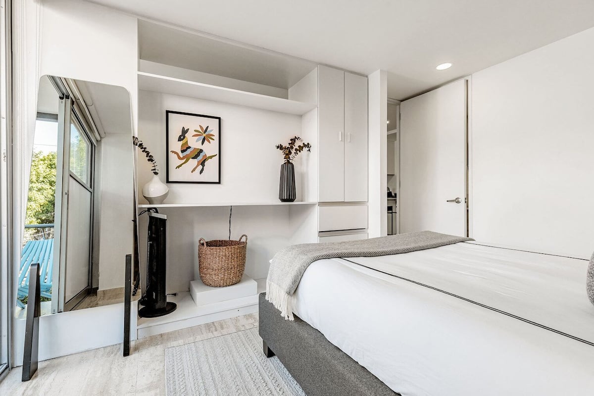 A modern bedroom with a bed, a bedside table, a mirror, a framed picture, and a basket.