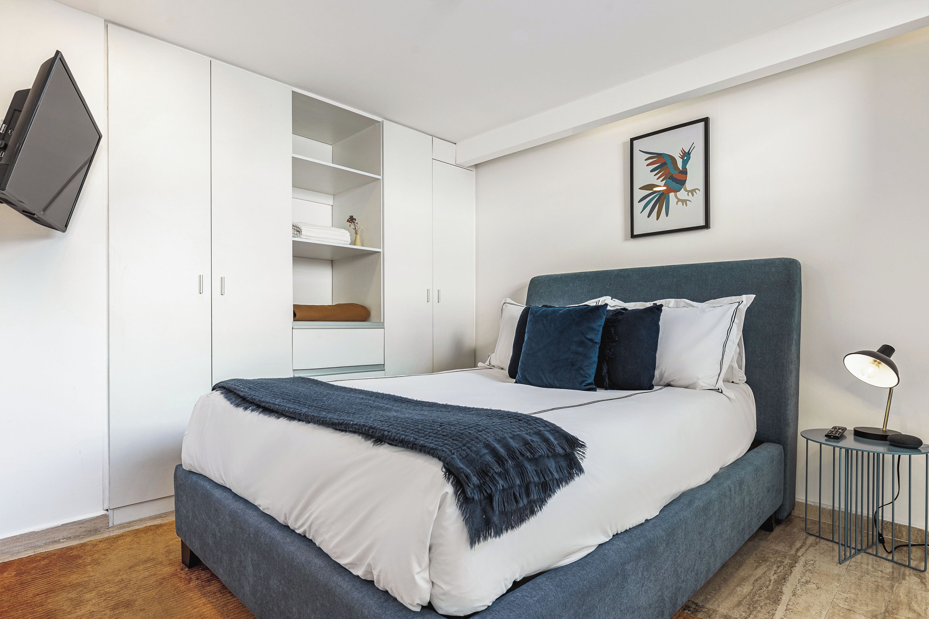 A modern bedroom with a bed, a wardrobe, a TV, and a framed artwork on the wall.