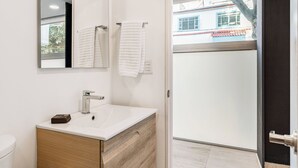 Un bany modern amb un rentapeus blanc, un armari de tocador de fusta i dues tovalloles blanques penjades a ganyixos.