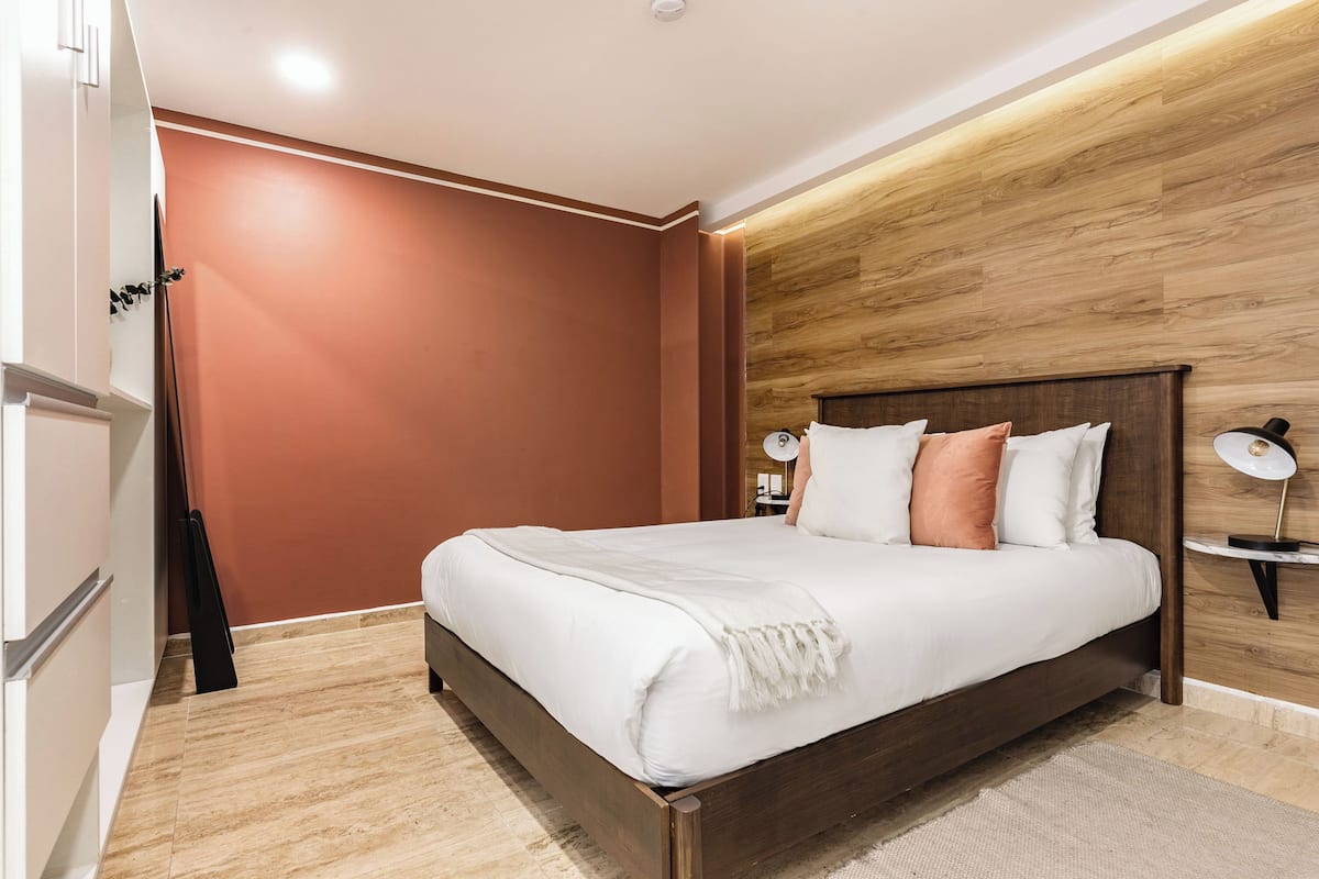 A modern bedroom with a wooden headboard, a large bed with white bedding, and a nightstand with a lamp.