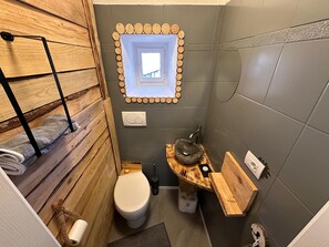 Pieni kylpyhuone, jossa on puinen allaskaappi, wc ja pieni ikkuna.