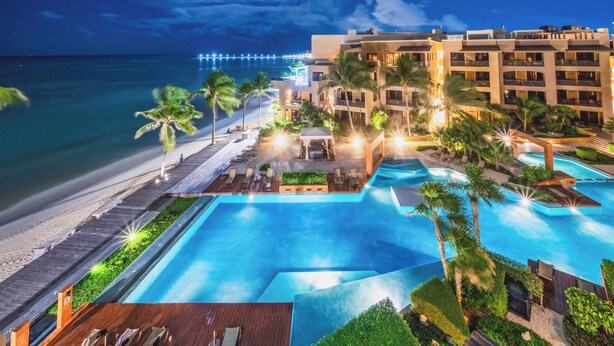 Un complexe hôtelier doté d’une grande piscine, de palmiers et offrant une vue sur la plage.
