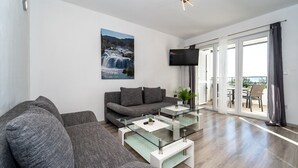 Ett modernt vardagsrum med en grå soffa, ett soffbord i glas och en stor TV på väggen.