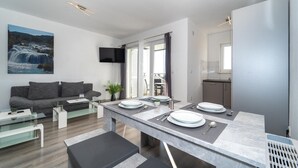 Ett modernt vardagsrum med en soffa, ett soffbord i glas och en matplats med ett marmorbord där fyra personer kan sitta.