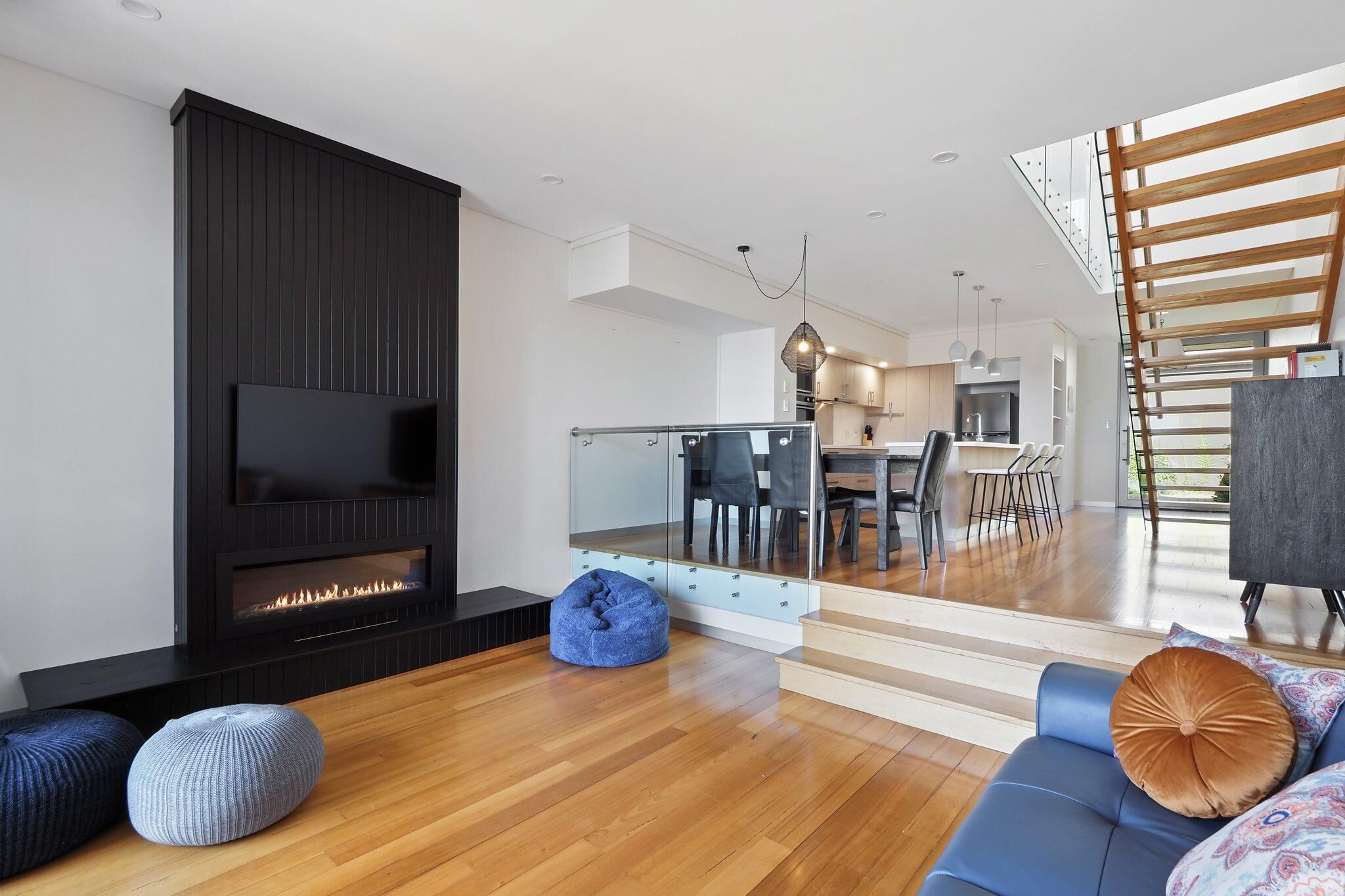 Una sala de estar moderna con chimenea, un sofá y un área de comedor visible a través de una pared de vidrio.