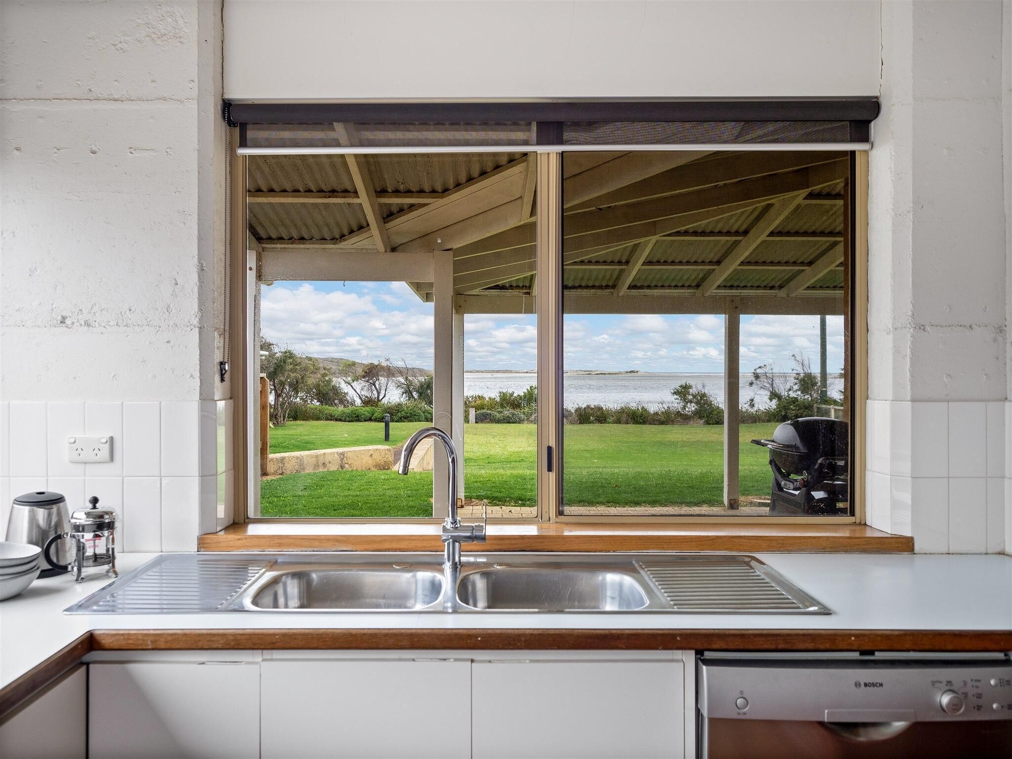 A kitchen with a large window, a Bosch dishwasher, and a view of a grassy area and water body.